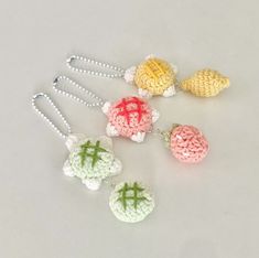 four crocheted fruits are shown on a white surface with silver chains and beads