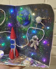 an open book with some space related items on it and a rocket ship in the middle