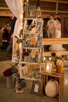 a ladder with pictures and flowers on it in front of a wedding reception table at the barn