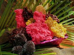 several different colored candies are in a basket on the ground next to palm leaves