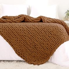 a bed with a brown blanket on top of it and white pillows in the background