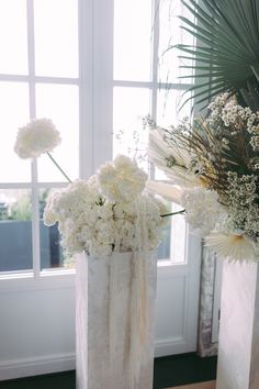 two vases filled with white flowers next to a window