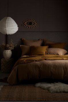 a bed with brown linens and pillows in a dark room next to a lamp