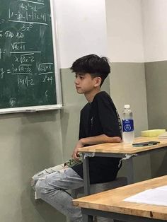 a young boy sitting at a desk in front of a chalkboard