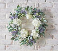 a wreath with white flowers and greenery on a brick wall