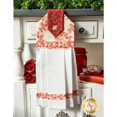 a red and white kitchen towel hanging on the wall next to a cabinet with flowers