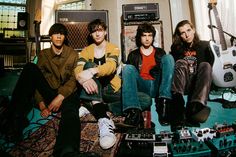 four young men sitting on the floor in front of guitars and amps