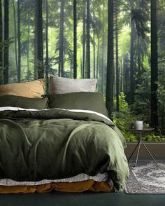 a bed with green sheets and pillows in front of a forest wall mural