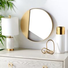 a round mirror sitting on top of a white dresser next to a lamp and potted plant