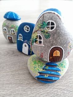 three rocks with houses painted on them sitting on a wooden table next to each other