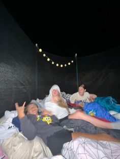 three people laying in bed with blankets on top of them and lights hanging from the ceiling