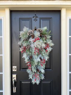 a christmas wreath on the front door of a house with pine cones, berries and holly