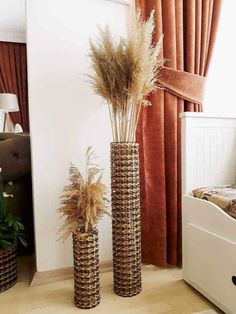 two tall vases with dried grass in them on the floor next to a bed