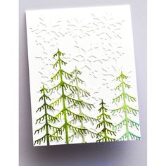 a white card with green pine trees on the front and bottom, which has been cut out to look like snowflakes