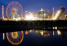 an amusement park at night with ferris wheel reflected in the water and lights reflecting on the ground