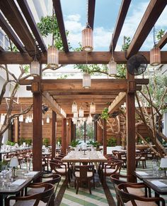 an outdoor dining area with wooden tables, chairs and hanging lanterns on the ceiling above them