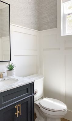 a white toilet sitting next to a sink in a bathroom under a mirror and a window