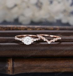 two wedding rings on top of a wooden table with white flowers in the back ground