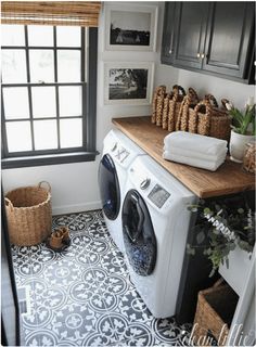 a washer and dryer in a small laundry room with black cabinets, wood counter tops, and patterned tile floor