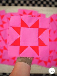 someone holding up a piece of pink paper with red squares on it and the background is black and white