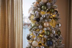 a decorated christmas tree with gold, silver and white ornaments in front of a window