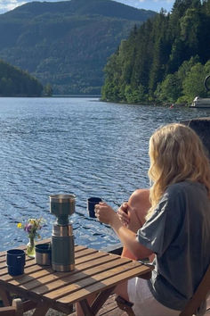 a woman sitting at a wooden table next to a lake