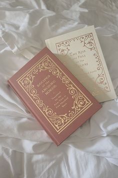 two books sitting on top of a bed next to each other, one is pink and the other is gold