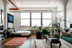 a living room filled with lots of furniture and plants on the floor next to a large window