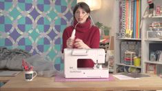 a woman is using a sewing machine to sew clothes on the table in front of her