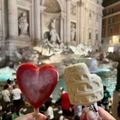 two heart shaped lollipops being held in front of a fountain