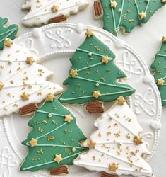 decorated christmas cookies on a white plate with gold stars and green frosted trees in the middle