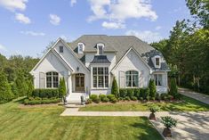 a large white house with lots of windows and bushes in front of the door is surrounded by green grass