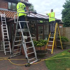 two men in yellow vests working on the roof of a house with ladders