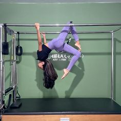 a woman is doing aerial acrobatic exercises on a metal bar in front of a green wall