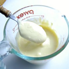 a glass measuring cup filled with yogurt and a wooden spoon