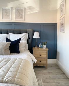 a bed with white and black pillows in a bedroom next to a night stand, lamp and pictures on the wall