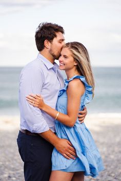 a man and woman standing next to each other on the beach with water in the background