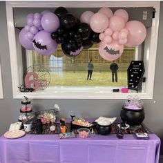 a purple table topped with lots of balloons and other items next to an open window