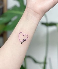 a small pink heart with an arrow tattoo on the left wrist, and a black bow in the middle