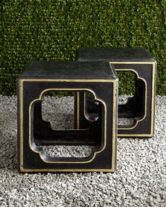 two black and gold side tables sitting next to each other on top of gravel covered ground