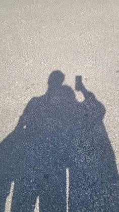 two people are standing in the street with their shadows on the ground and one is holding a skateboard