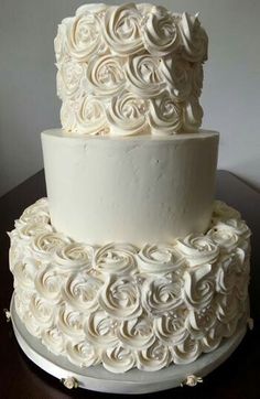 a three tiered cake with white frosting roses