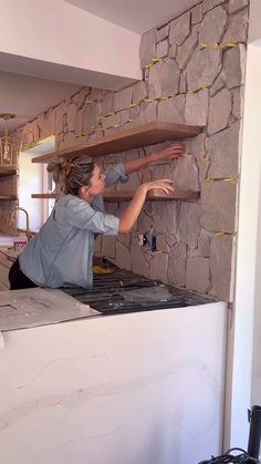 a woman sitting on top of a counter in front of a stone wall and shelves