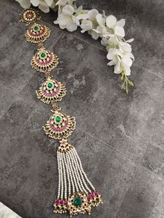 an elaborate necklace with green and pink stones on it, next to white orchids