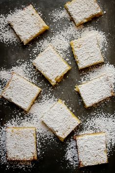 several pieces of cake with powdered sugar on top sitting on a black tablecloth