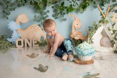 a baby is sitting on the floor next to a cupcake with blue frosting