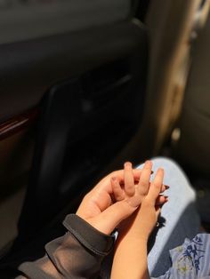 a small child sitting in the back seat of a car with their hands on someone's lap