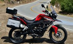 a red and black motorcycle parked on the side of a road next to a hill