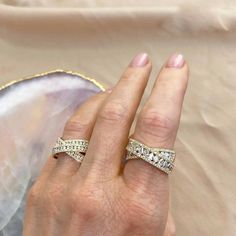 a woman's hand with two wedding bands on her finger and an oval shell in the background