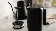 a black coffee pot sitting on top of a counter next to a cup and saucer